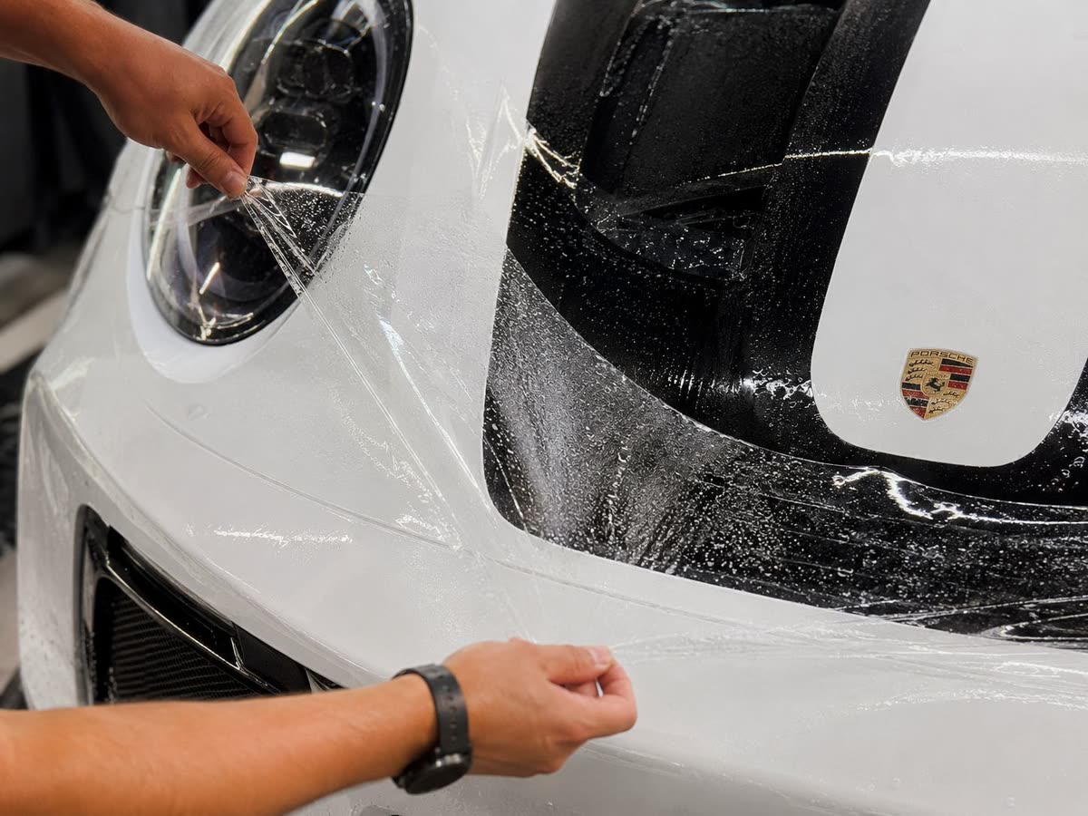 Installer applying paint protection film to a white Porsche front end